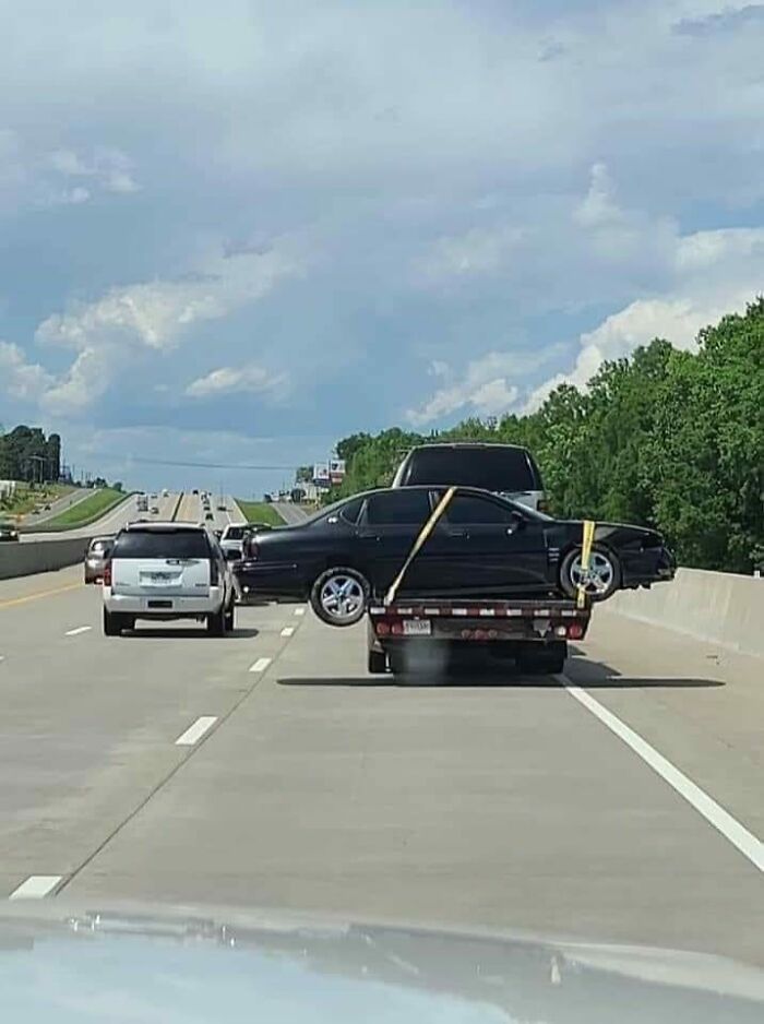 Car precariously balanced on trailer, defying OSHA safety regulations, while being transported on a busy highway.