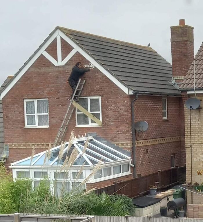 Person balancing precariously on a ladder while repairing a house roof, ignoring OSHA safety regulations.