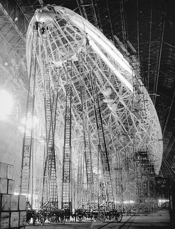 Unsafe construction scene with multiple tall ladders inside an airship framework, disregarding OSHA safety regulations.