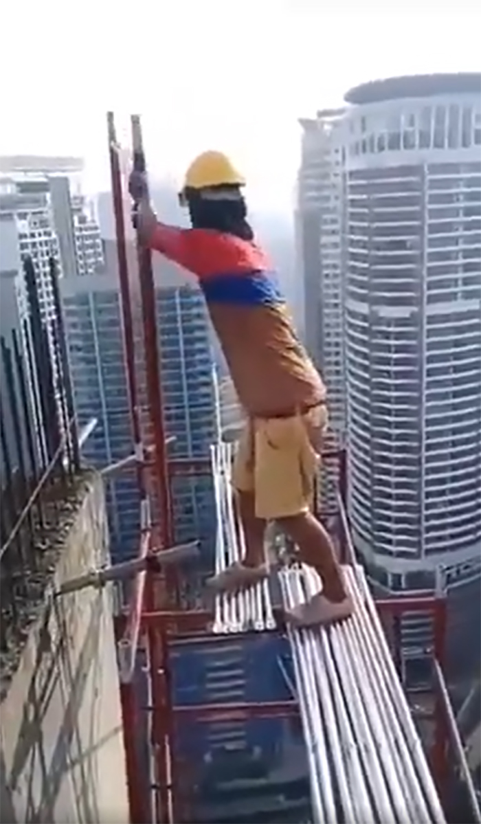 Worker standing unsafely on scaffolding at high-rise construction site, overlooking city skyline, ignoring OSHA safety regulations.