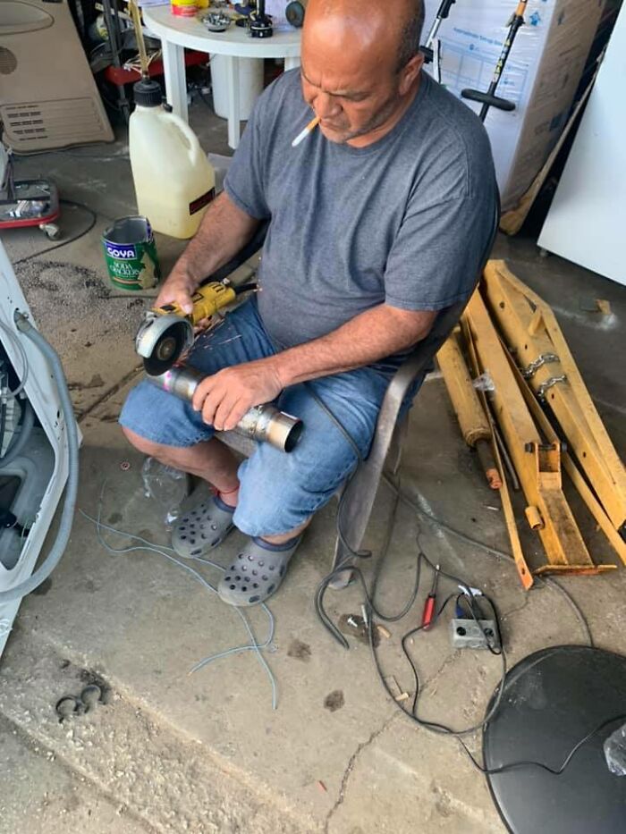 Man using an angle grinder on a pipe in a workshop, not following OSHA safety regulations, cigarette in mouth.