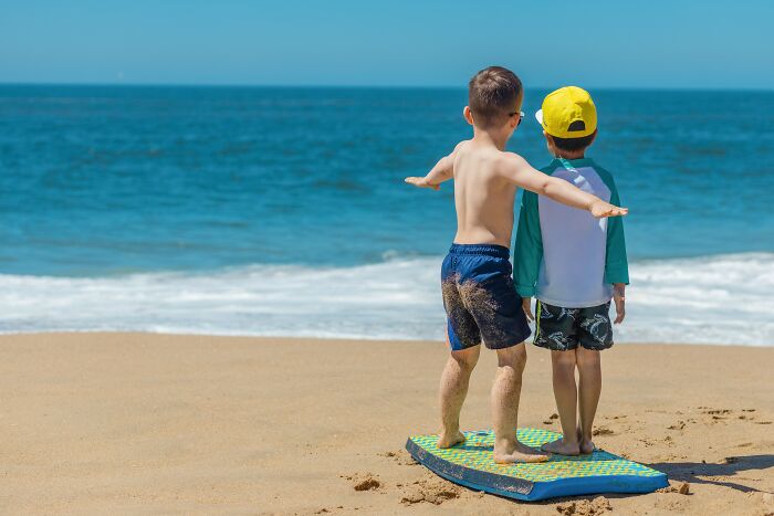 Two Kids On A Paddle Board On Sand 