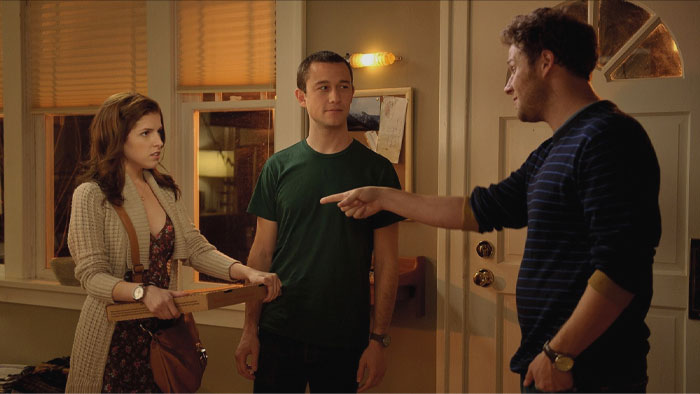 Two men and a woman standing and one man pointing at woman's pizza box 