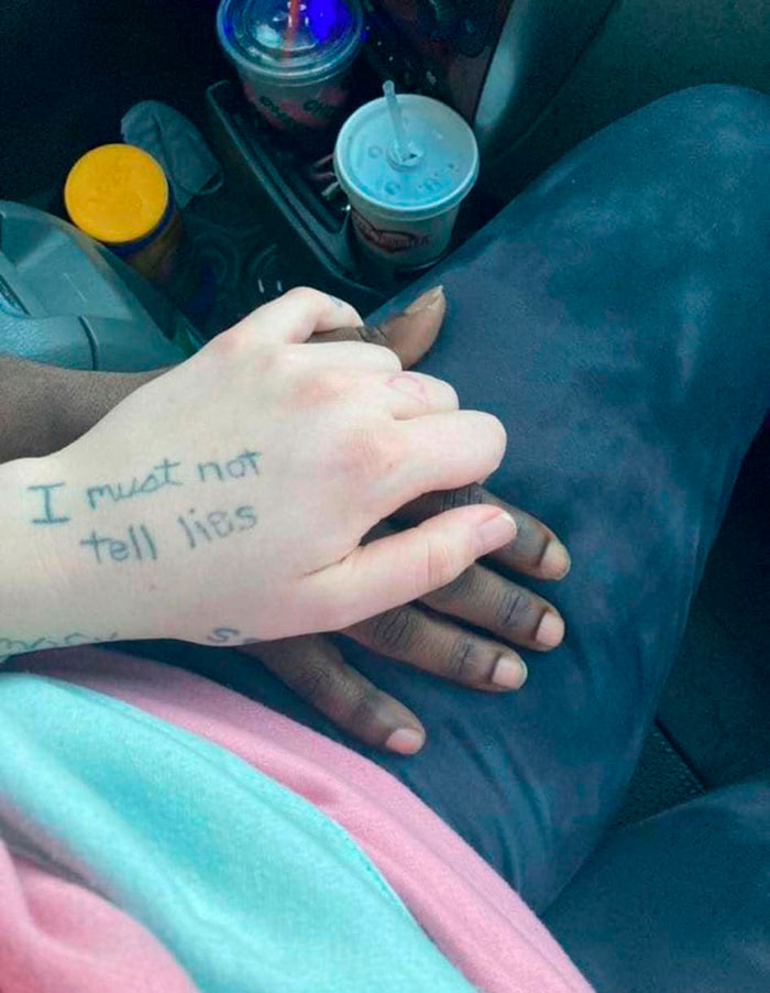Hand tattoo reads "I must not tell lies," shown while holding hands in a car setting.