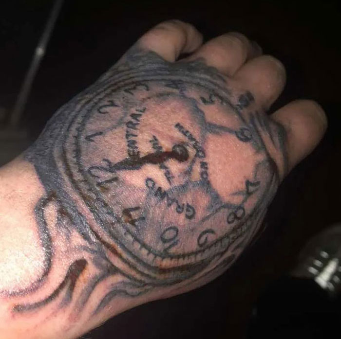 Poorly done clock tattoo covers a person's hand, numbers and design appear distorted.