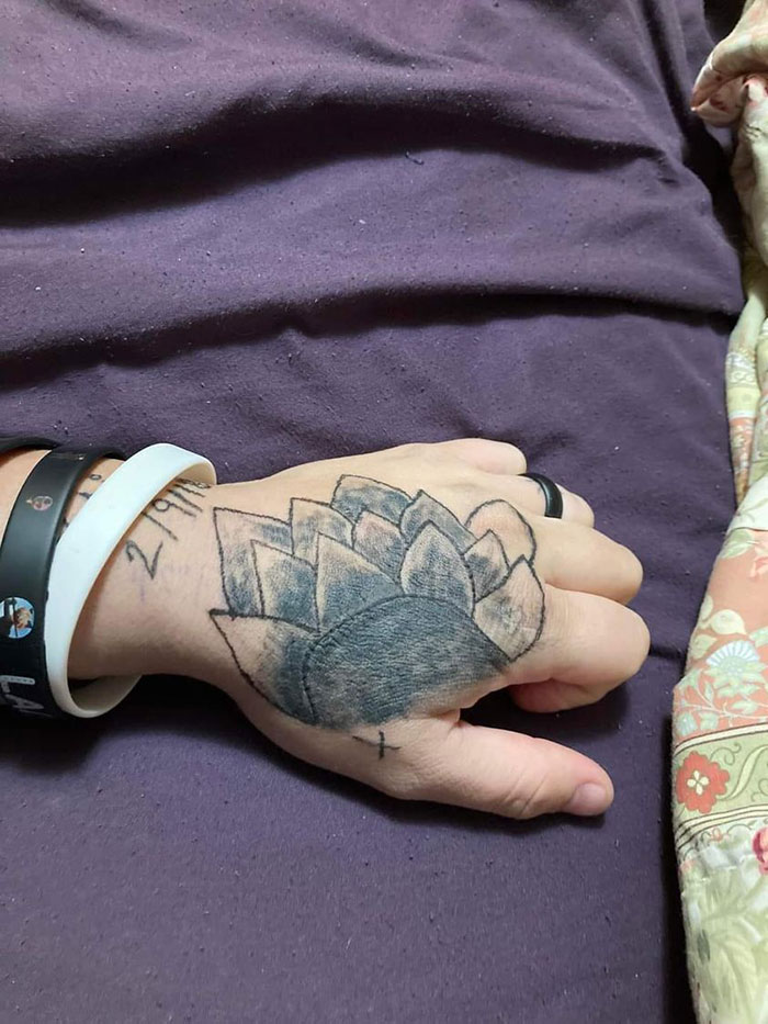 Hand with a poorly drawn flower tattoo on the back, lying on a purple blanket.