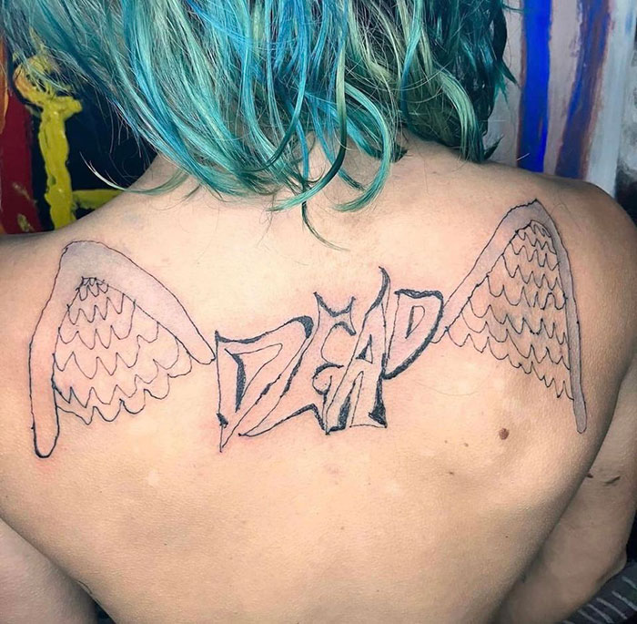 Person with a poorly designed tattoo of wings and the word "dead" on their back, highlighting bad tattoo art.