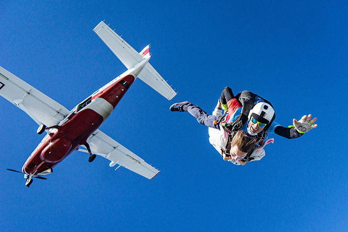 Person skydiving solo, capturing a "me time" adventure, freefalling near a small plane against a clear blue sky.