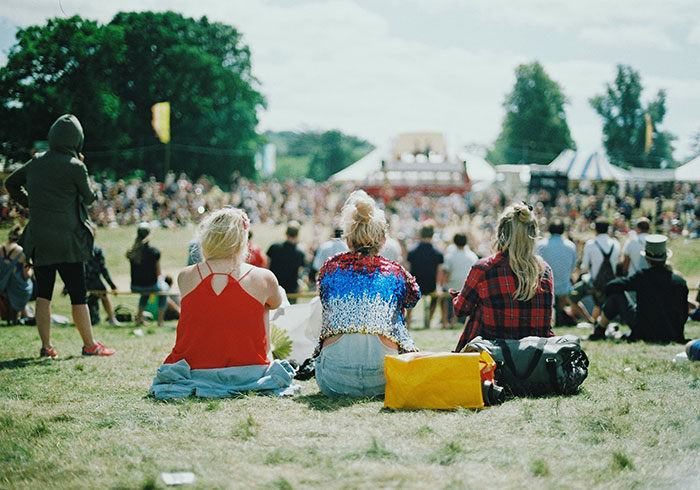 Person enjoying "me time" at a festival, sitting on grass, surrounded by a crowd.