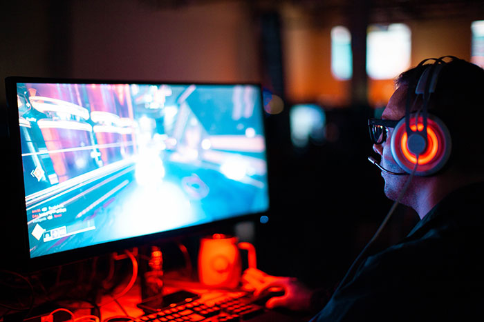 Person enjoying a video game alone, wearing headphones, with a glowing monitor, embracing "me time" activities.