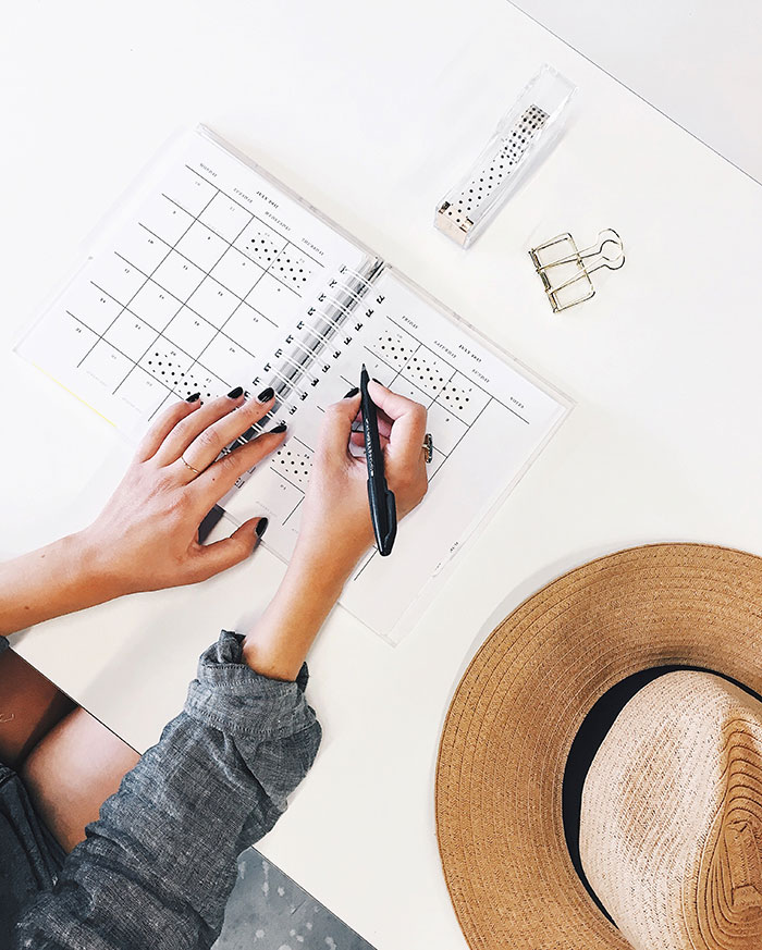 Person organizing a calendar alone, pen in hand, while enjoying some "me time." Hat and office supplies nearby.