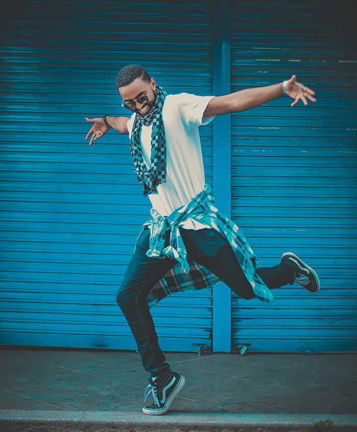 Person enjoying dancing alone, wearing casual attire, showcasing a dynamic pose against a blue shutter background.