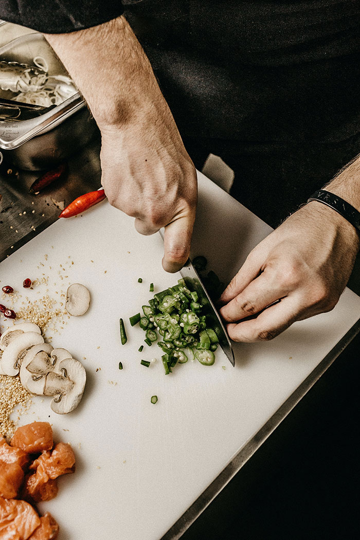 Person preparing ingredients on a cutting board, focusing on cutting green onions, showcasing a solo cooking activity.