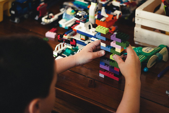Child engaging in "me time" by building a model with LEGO bricks on a wooden table.