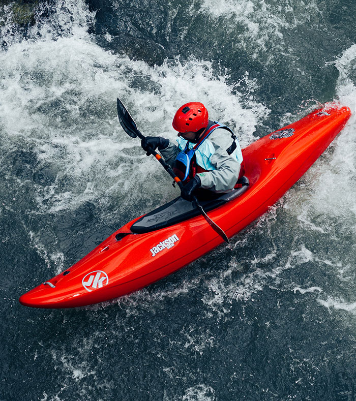 Person kayaking alone on a river, enjoying "me time" in a red kayak with safety gear and a paddle.