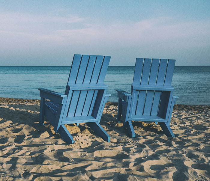 Two blue chairs on sandy beach, perfect for enjoying "me time" by the ocean.