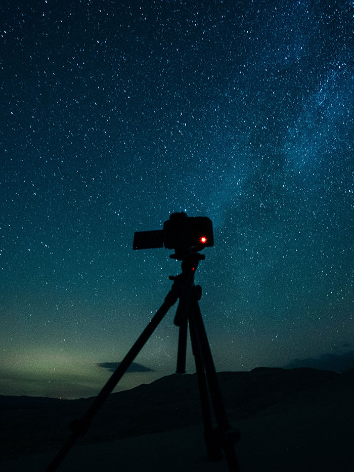 Night sky full of stars with a silhouette of a camera on a tripod, perfect for relaxing me time activities.