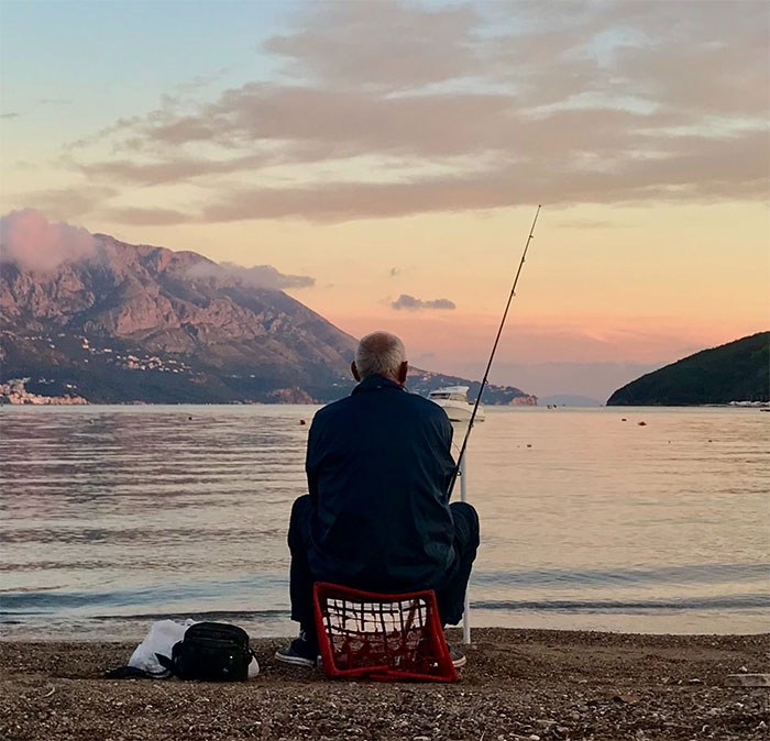 Person enjoying some me time fishing alone by the peaceful lakeside at sunset.