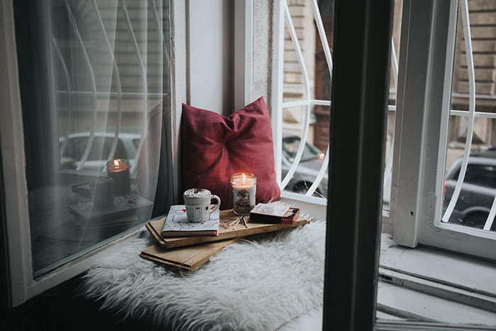 Cozy “me time” setting with coffee, books, and pillow by a window.