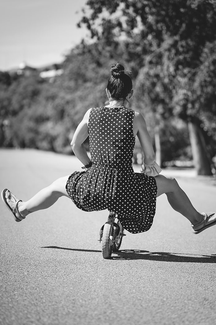 Woman enjoying some me time riding a mini bike on an empty road, wearing a polka dot dress.