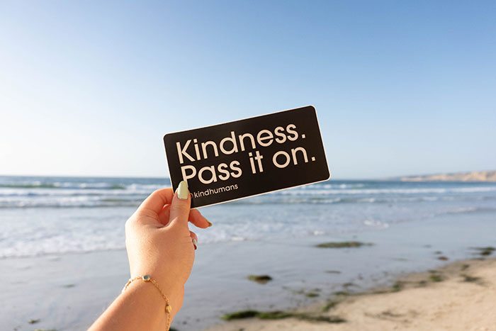 Person holding a card with "Kindness. Pass it on." message, ideal for solo reflection during "me time."