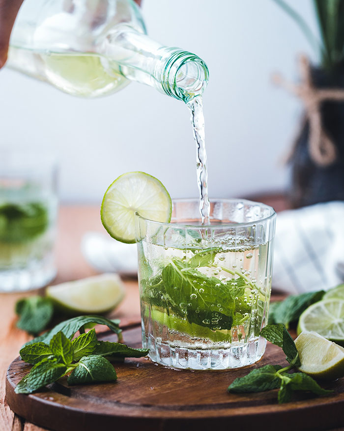 Person pouring a cocktail with lime and mint, capturing a moment of "me time" relaxation.