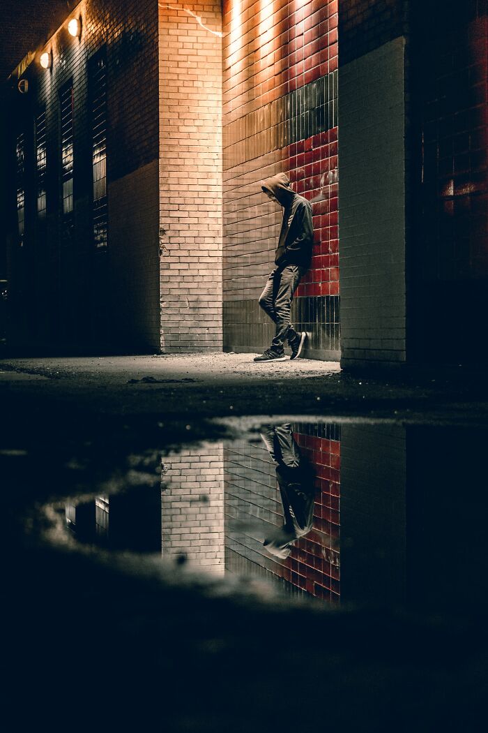 Person in a hoodie standing alone in dimly lit alley with reflection in puddle, illustrating worst birthdays ever feeling.