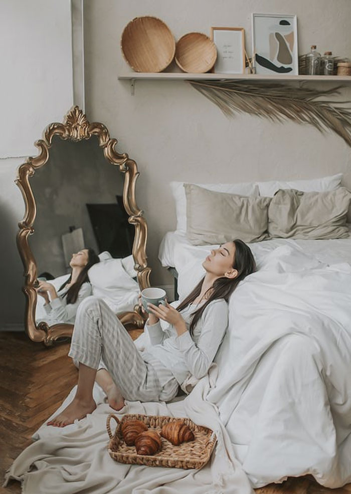 Woman in pajamas sitting and eating near a bed 