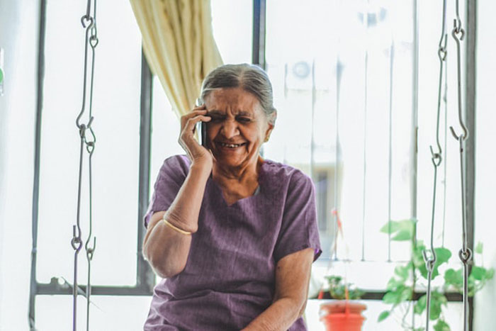 Elderly woman laughing while talking on phone indoors, illustrating people having the worst birthdays ever in a shared online thread.