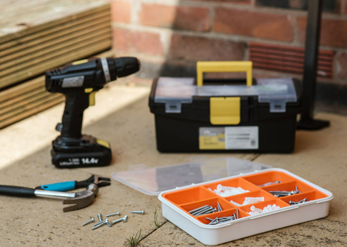 Cordless drill, toolbox, and hardware components on a patio, representing dads sharing homeowning knowledge.
