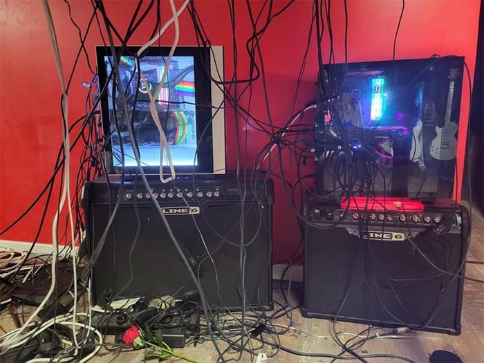 Two PC gaming setups with illuminated components tangled in numerous black and white cables against a red wall, showcasing cursed gaming setups.