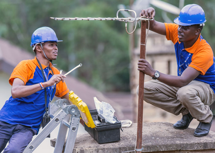 Two men in safety helmets working together on homeowning repairs outdoors with tools and equipment.