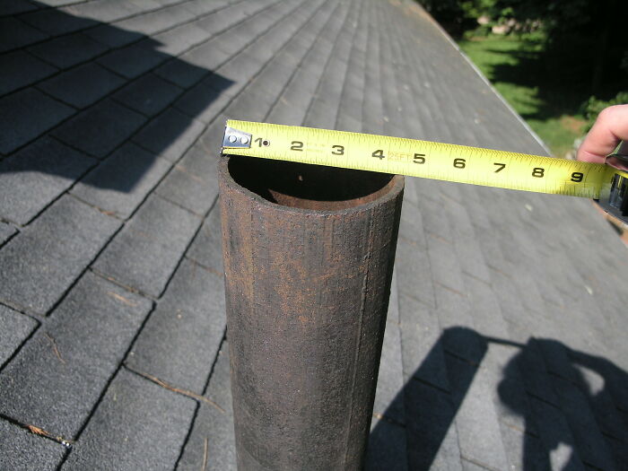 Measuring the diameter of a rusty metal pipe on a roof, highlighting basic facts noticed by many individuals.