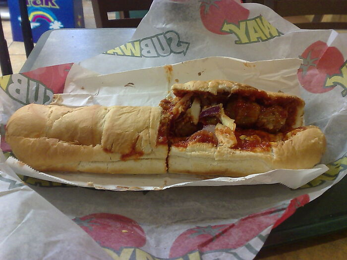 Partially eaten Subway sandwich with meatballs and sauce on branded wrapping in a casual dining setting.
