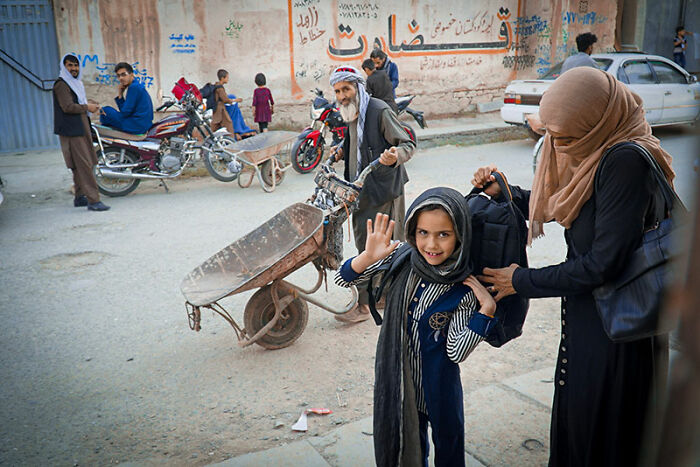 Afghan street scene with people, motorcycles, and a smiling girl waving, showing life while traveling in Afghanistan.