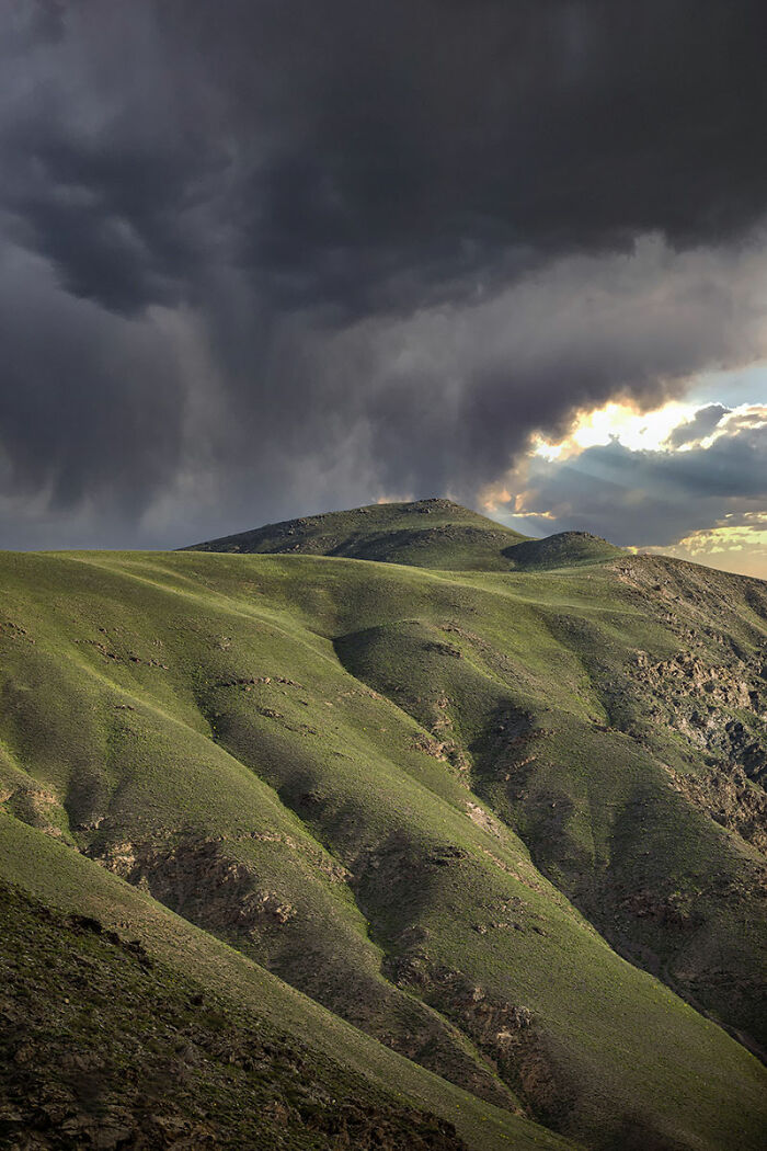 Green rolling hills under dark storm clouds showcasing Afghanistan's dramatic and scenic natural landscape during travel.