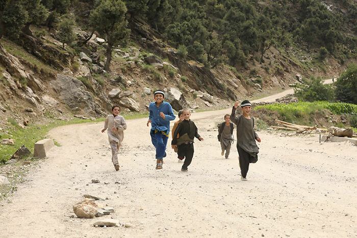 Children running joyfully on a rural road in Afghanistan, showcasing daily life and scenic mountainous surroundings while traveling.