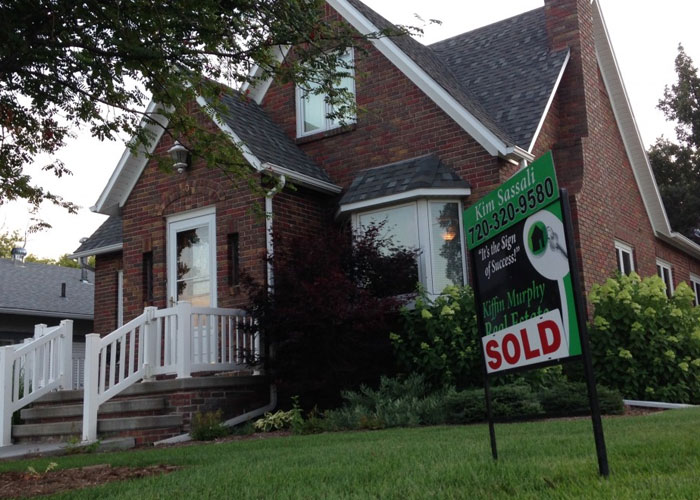 Brick house with sold sign on lawn, representing dads sharing homeowning knowledge in a real estate context.