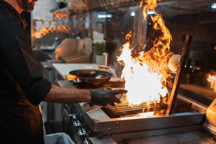 Chef in a commercial kitchen managing a large flame on the grill, highlighting people noticing basic facts about cooking safety.