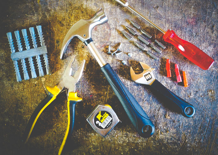 Various homeowning tools including hammer, pliers, screwdriver, wrench, and measuring tape arranged on a worn surface.