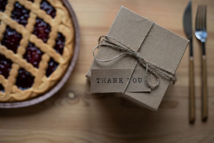 Brown gift box tied with twine and thank you tag next to a berry pie and wooden utensil set on table, highlighting basic facts.
