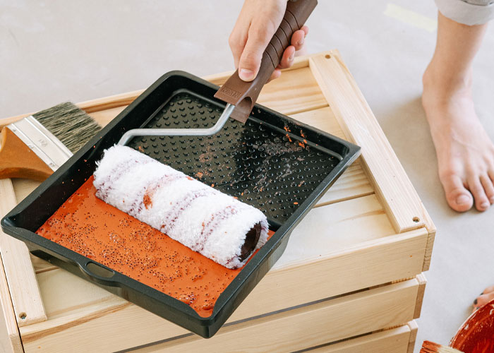 Paint roller being dipped into a tray with red paint, illustrating dads sharing knowledge about homeowning tips and techniques.