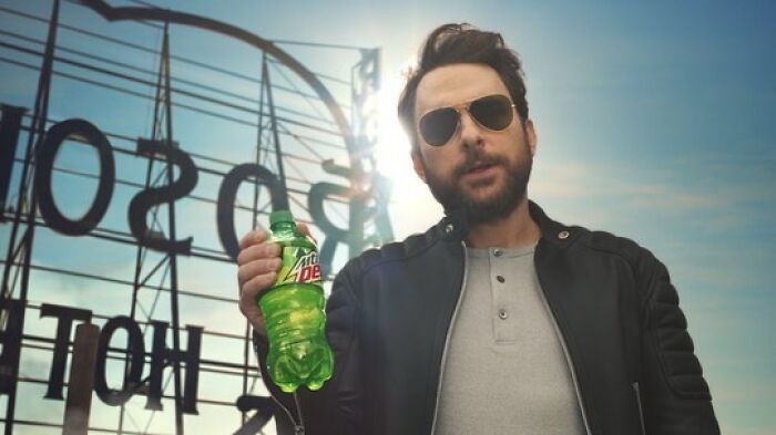 Man wearing sunglasses and a leather jacket holding a Mountain Dew bottle, representing smartest celebrities with intelligence.
