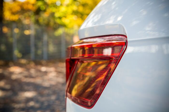 Close-up of a white car's rear light surrounded by blurred autumn trees, highlighting details noticed by individuals.