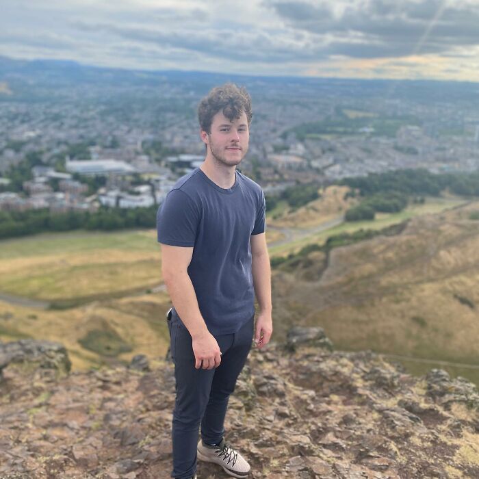 Young man standing on rocky hilltop overlooking cityscape, representing smartest celebrities known for intelligence and talent.