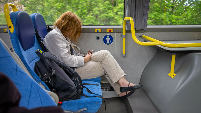 Person sitting alone on a bus, looking at their phone, illustrating people noticing others not knowing basic facts.