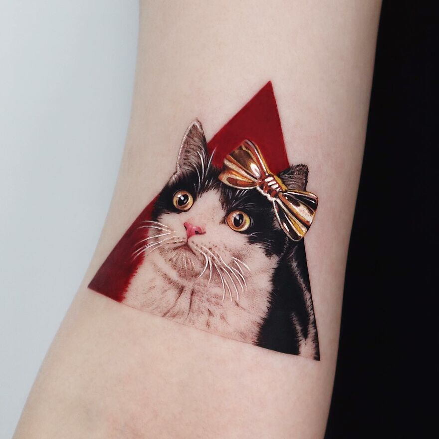 Golden tattoo of a cat with a bow, designed by Manhattan-based tattoo artist, showing precision and artistry.