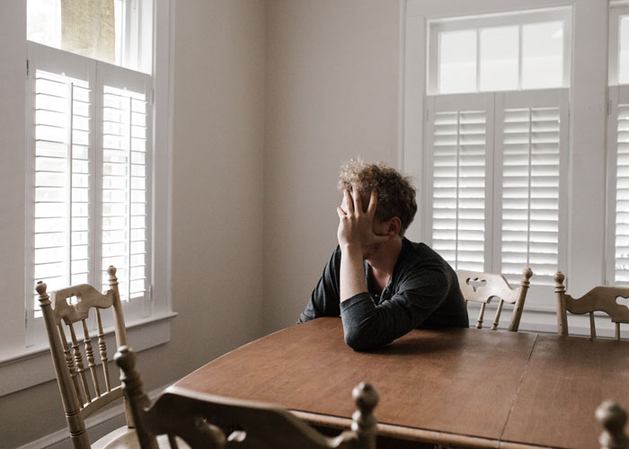 Man sitting alone at a wooden table, appearing distressed, reflecting disturbing things experienced while at work.