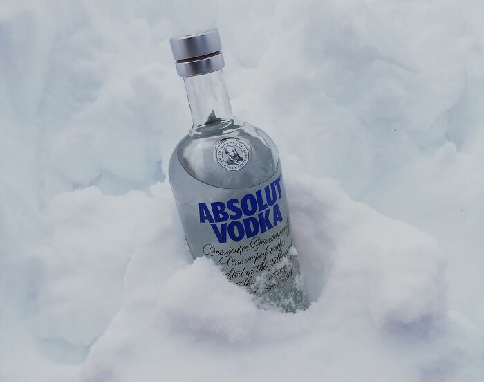 Clear Absolut Vodka bottle partially buried in soft snow, illustrating surprising facts many people have not noticed.