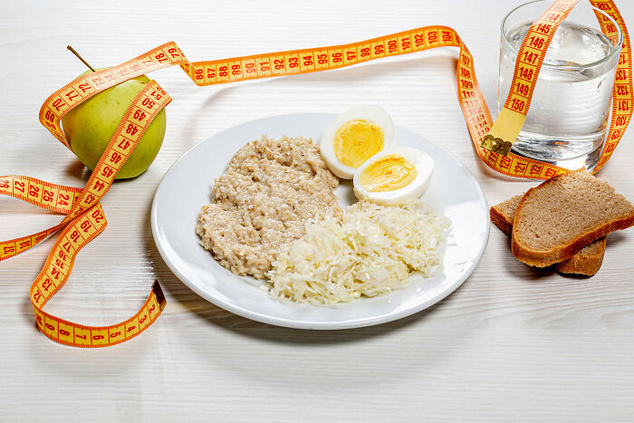 Plate with boiled egg, porridge, and sauerkraut next to apple, bread, and measuring tape symbolizing basic facts on nutrition.